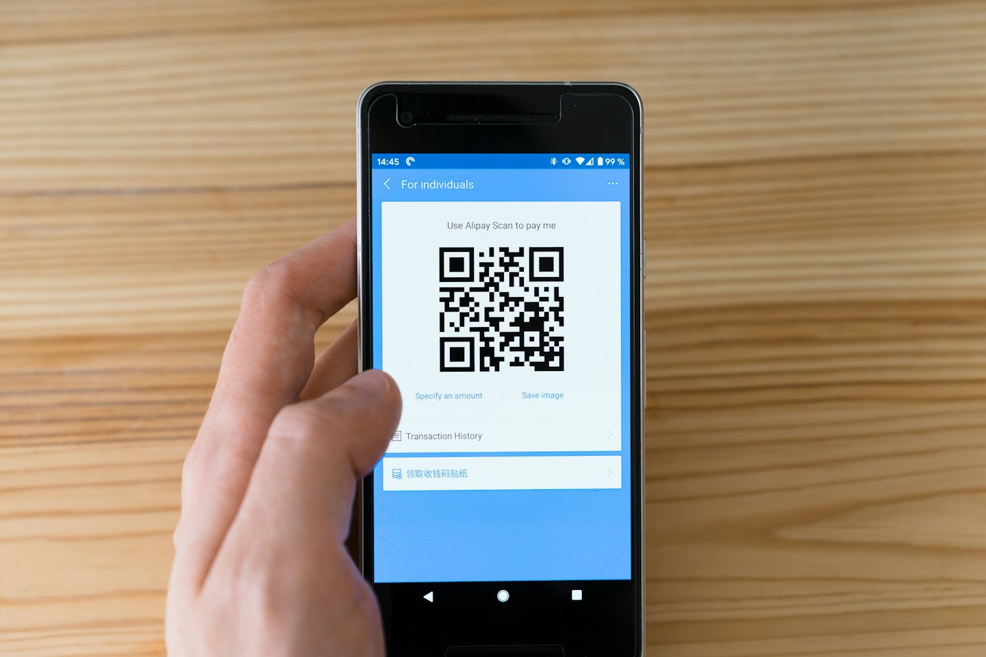 Käsi hoiab nutitelefoni makserakenduse QR-koodiga puidust laual.
